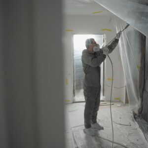 Man in protective gear spray painting a house's interior during renovation work. - Photo by Tima Miroshnichenko on Pexels