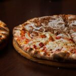 Close-up of two delicious pizzas with pepperoni and onions on a wooden table. - Photo by pedro furtado on Pexels