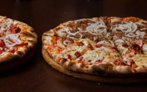 Close-up of two delicious pizzas with pepperoni and onions on a wooden table. - Photo by pedro furtado on Pexels
