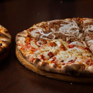 Close-up of two delicious pizzas with pepperoni and onions on a wooden table. - Photo by pedro furtado on Pexels